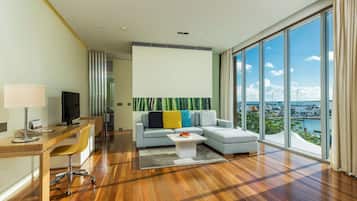 A modern living room with a large window, a sofa, a coffee table, and a desk with a lamp and a television.