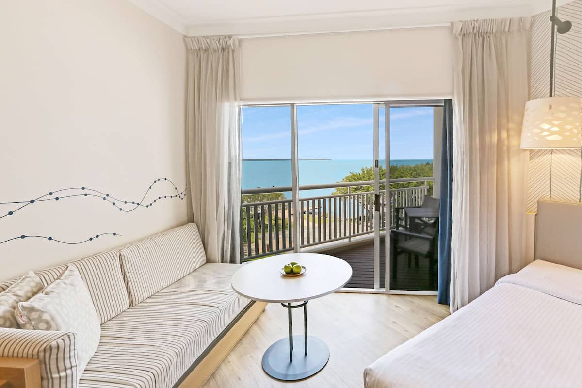 Una habitación de hotel con balcón, sofá, una mesita y cama.