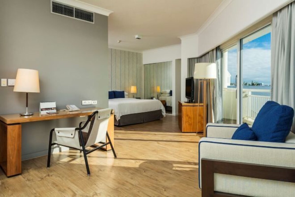 A hotel room with a desk, chair, bed, TV, and a balcony with a view.