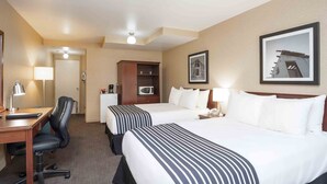 A hotel room with two beds, a desk with a chair, a microwave, a wardrobe, and a framed picture on the wall.