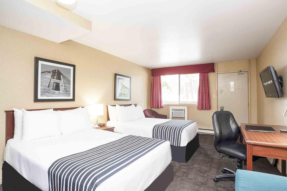 A hotel room with two beds, a desk, a chair, a television, and framed pictures on the wall.
