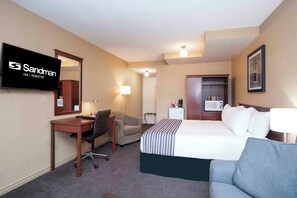 A hotel room with a bed, a desk, a chair, a TV, a lamp, and a microwave.