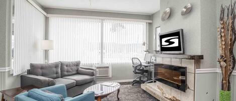 A living room with a grey sofa, blue armchairs, a coffee table, a fireplace, and a TV mounted on the wall.