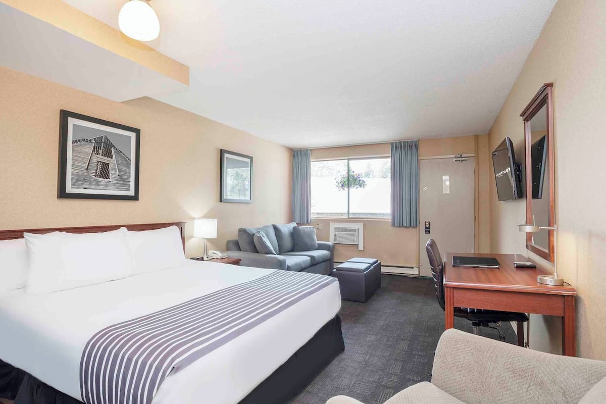 A hotel room with a large bed, a desk, a chair, a sofa, a TV, and a window with curtains.