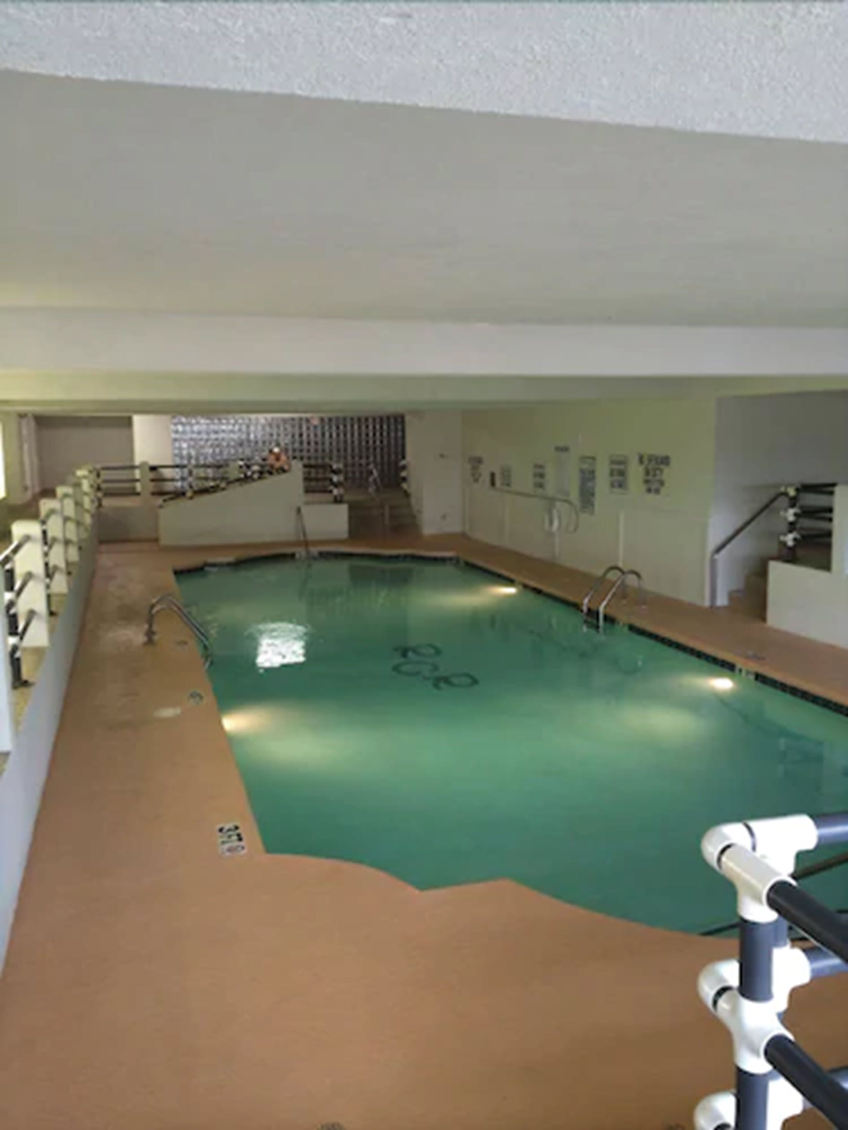 Piscina interior com trampolim, escadas para um vestiário e parede revestida com janela.