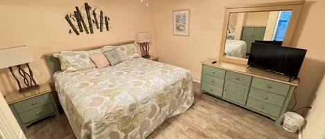 Quarto com cama, mesas de cabeceira, cômoda, televisão e espelho.