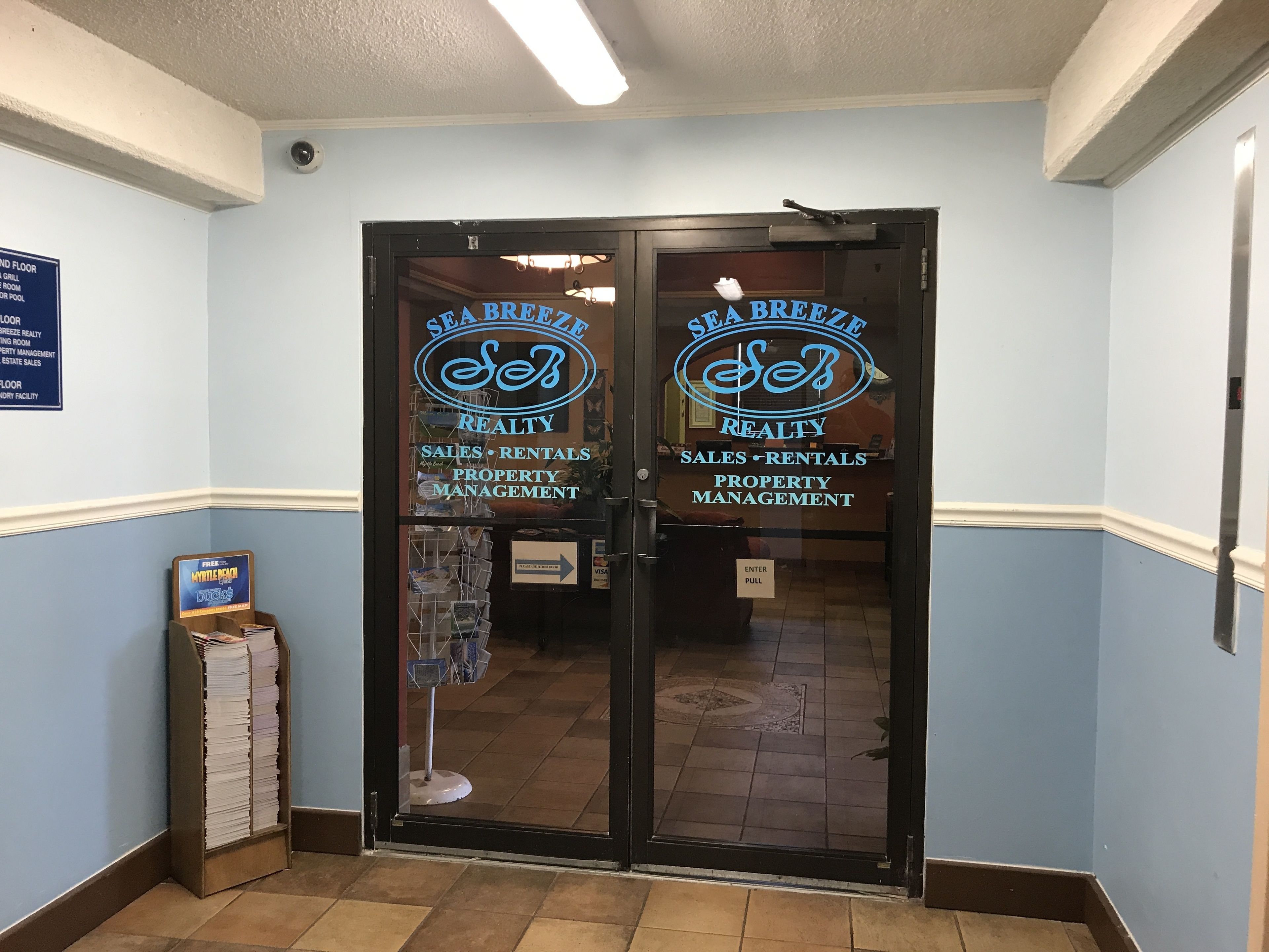 A double door entrance with 'Sea Breeze Realty' signage, a 'Free' sign, and a 'VISA' sign.