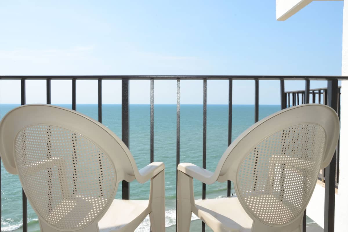 Two white chairs with perforated backs facing a balcony with a view of the sea.