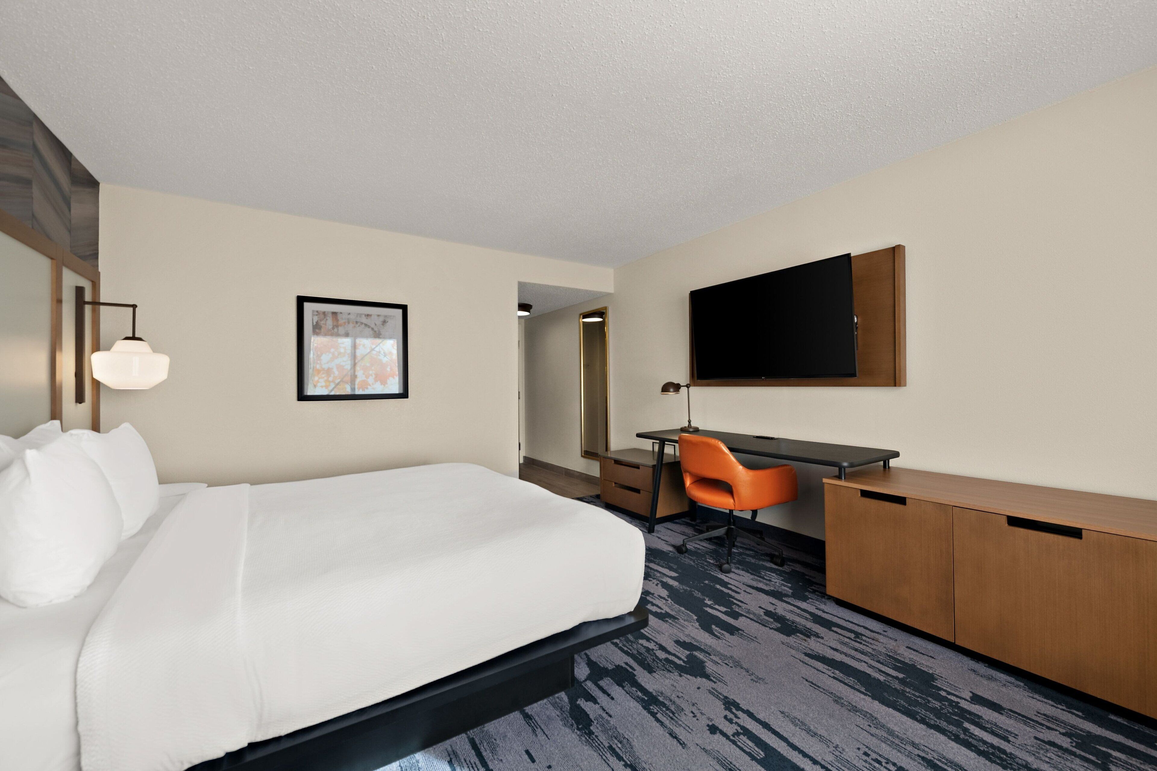 A hotel room with a bed, desk, chair, and a flat-screen TV on the wall.