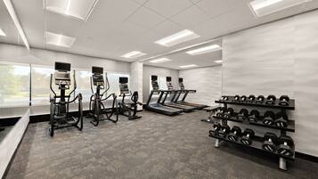 Et moderne fitnesscenter med løbebånd, crosstrainere og et stativ med håndvægte.