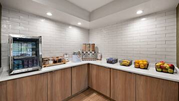 A kitchen area with a refrigerator, coffee machine, and various food items on the counter.