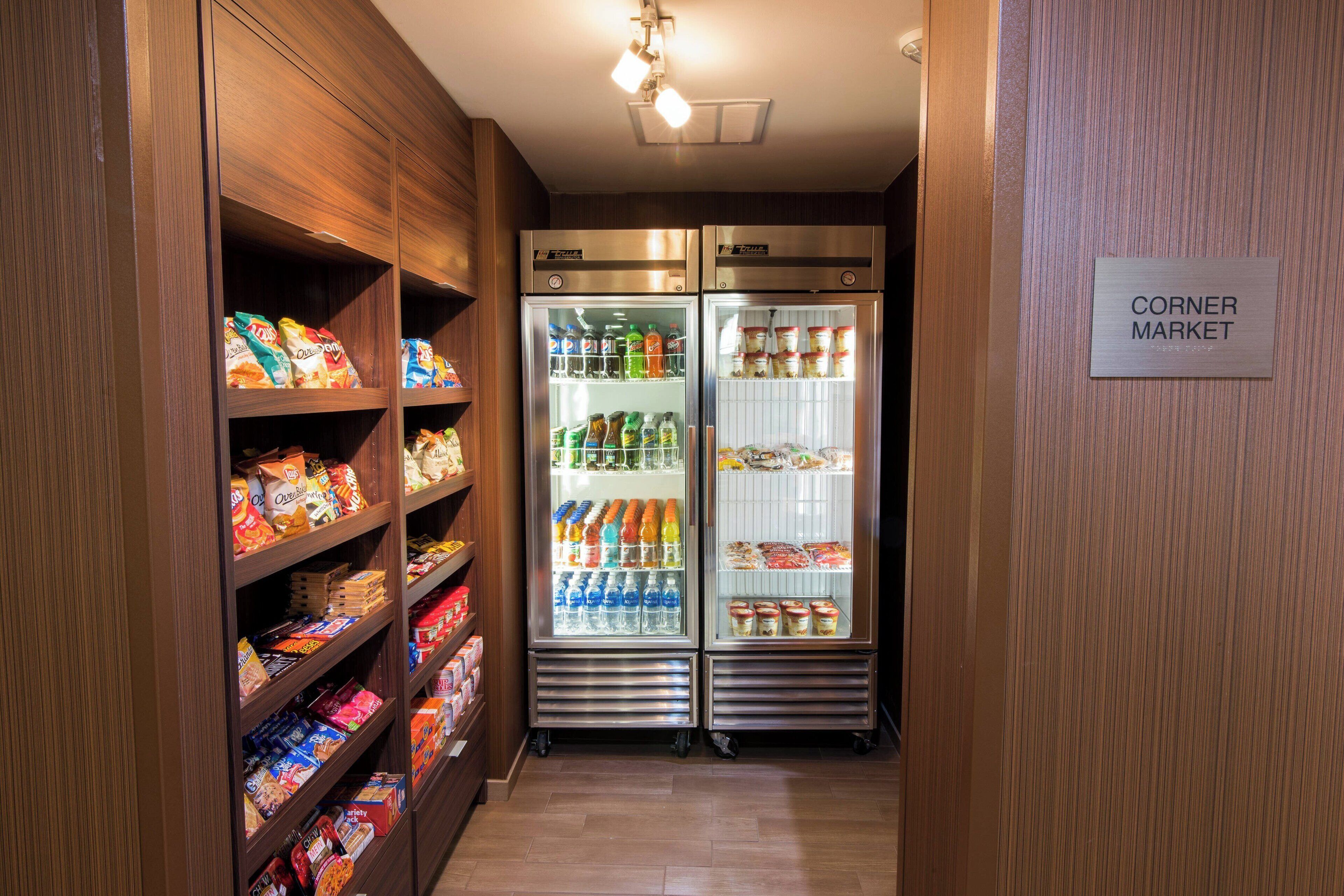 A corner market with shelves stocked with snacks and beverages, and two refrigerators.