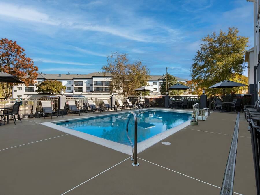 A rectangular outdoor swimming pool with a metal ladder, surrounded by lounge chairs and umbrellas.