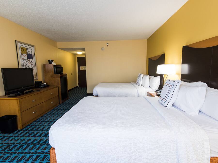Habitación de hotel con dos camas, un televisor sobre una cómoda de madera, un cesto de basura y una lámpara en la mesita de noche.