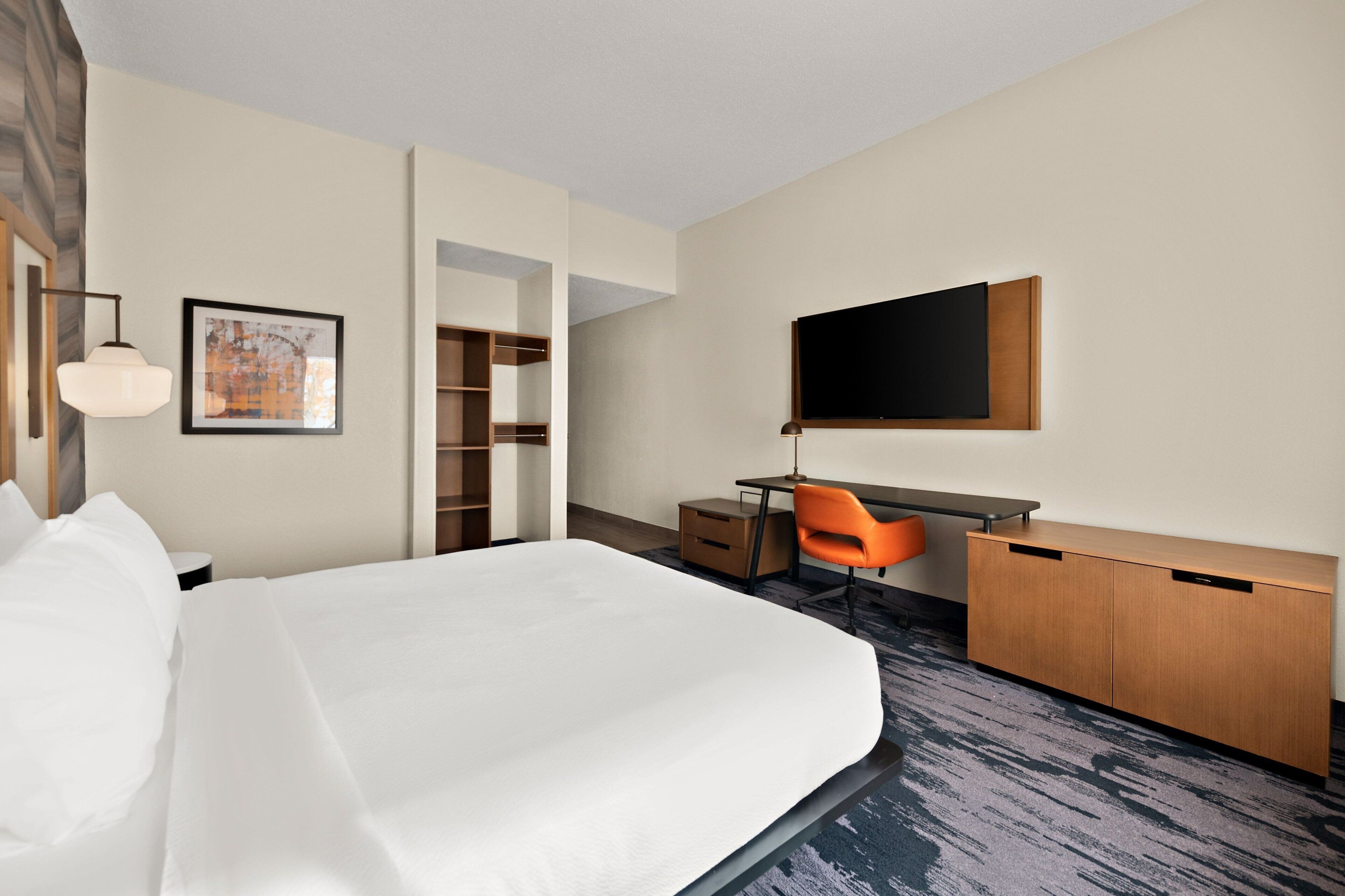 Een hotelkamer met een groot bed, een bureau met stoel, een televisie en een kledingkast.