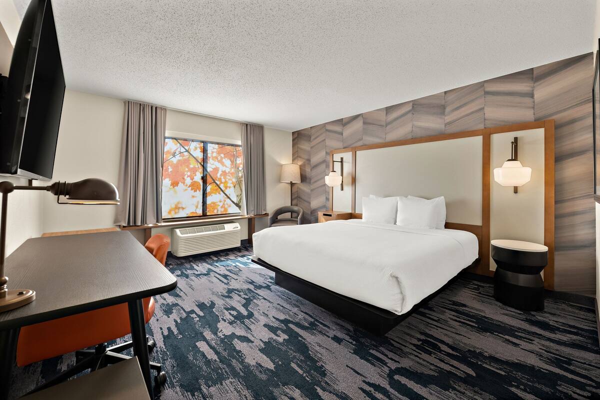 A hotel room with a large bed, a desk with a chair, a television, and a window with curtains.