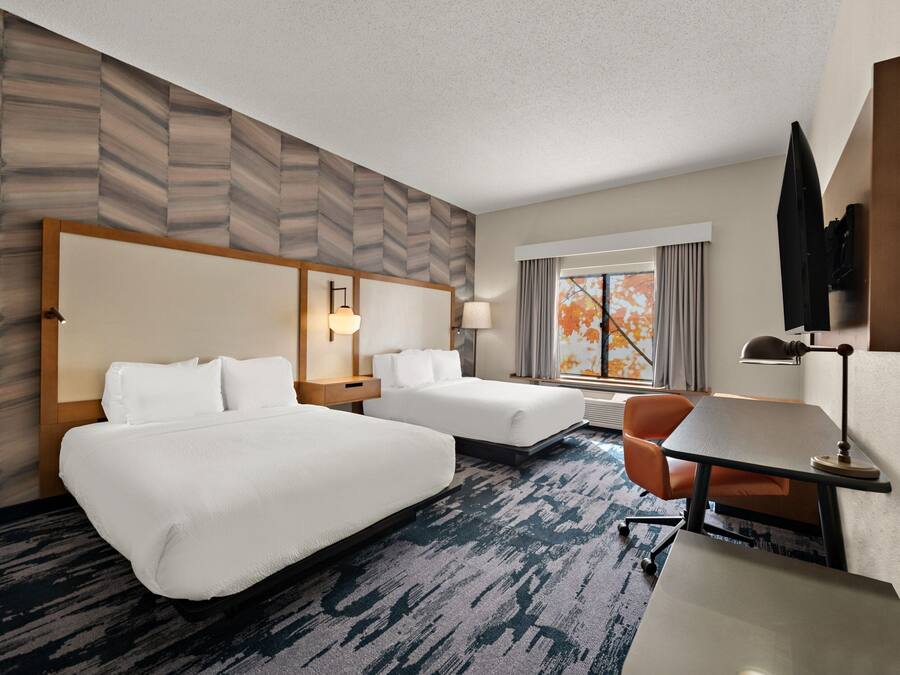A hotel room with two beds, a desk, a chair, a TV, and a window with curtains.
