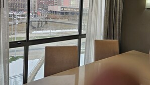 A modern hotel room with a large window offering a view of the cityscape, a round ceiling light, and a dining area with a table and chairs. - Wyndham Rochester Downtown (Rochester)