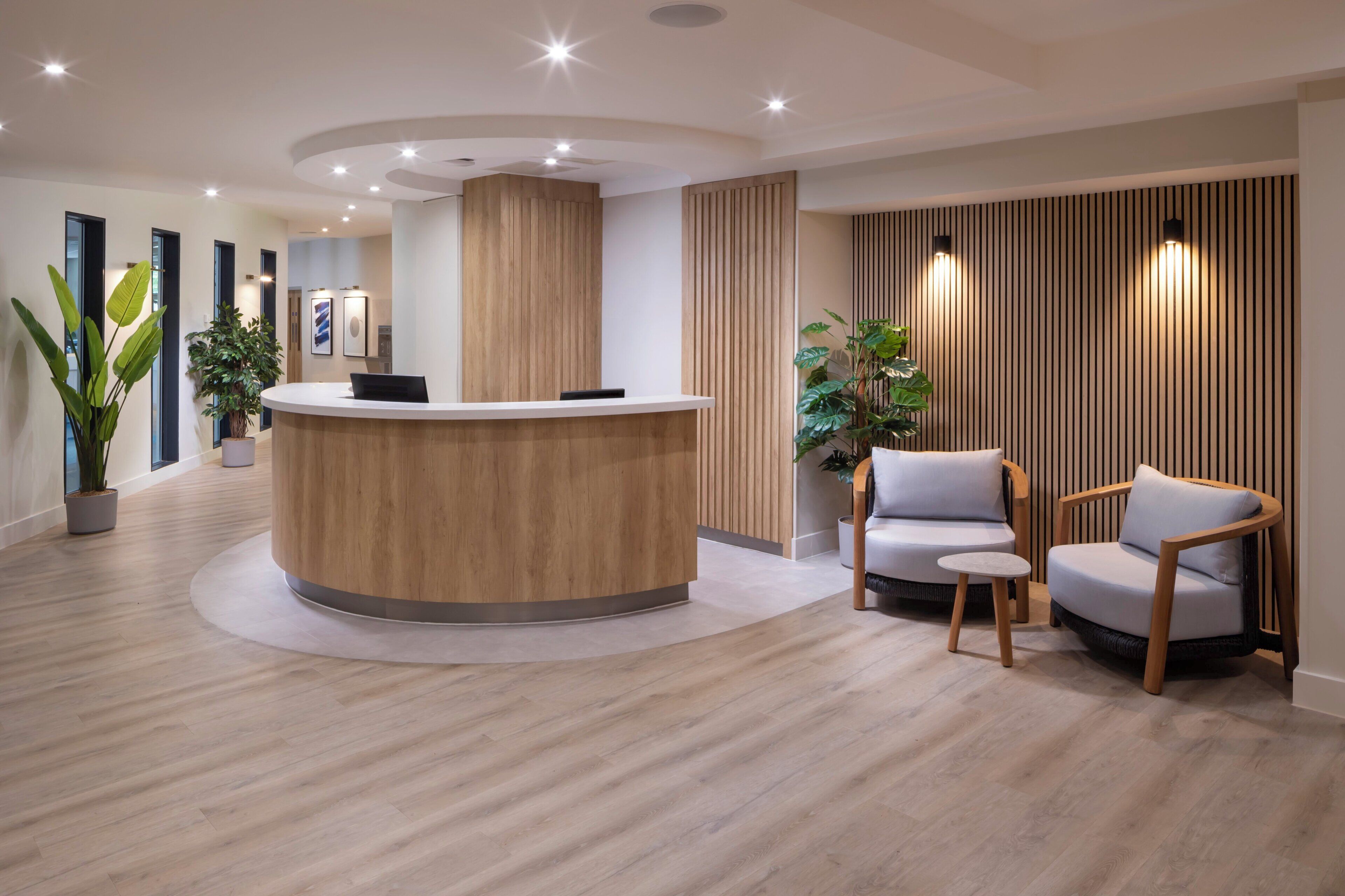 A reception area with a wooden reception desk, two chairs, potted plants, and a wall with vertical slats.