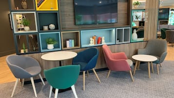 Un área de descanso moderna con televisor, sillas coloridas y estanterías con diversos objetos.