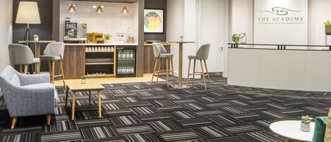 A modern hotel lobby with a reception desk, seating area, and a kitchenette.