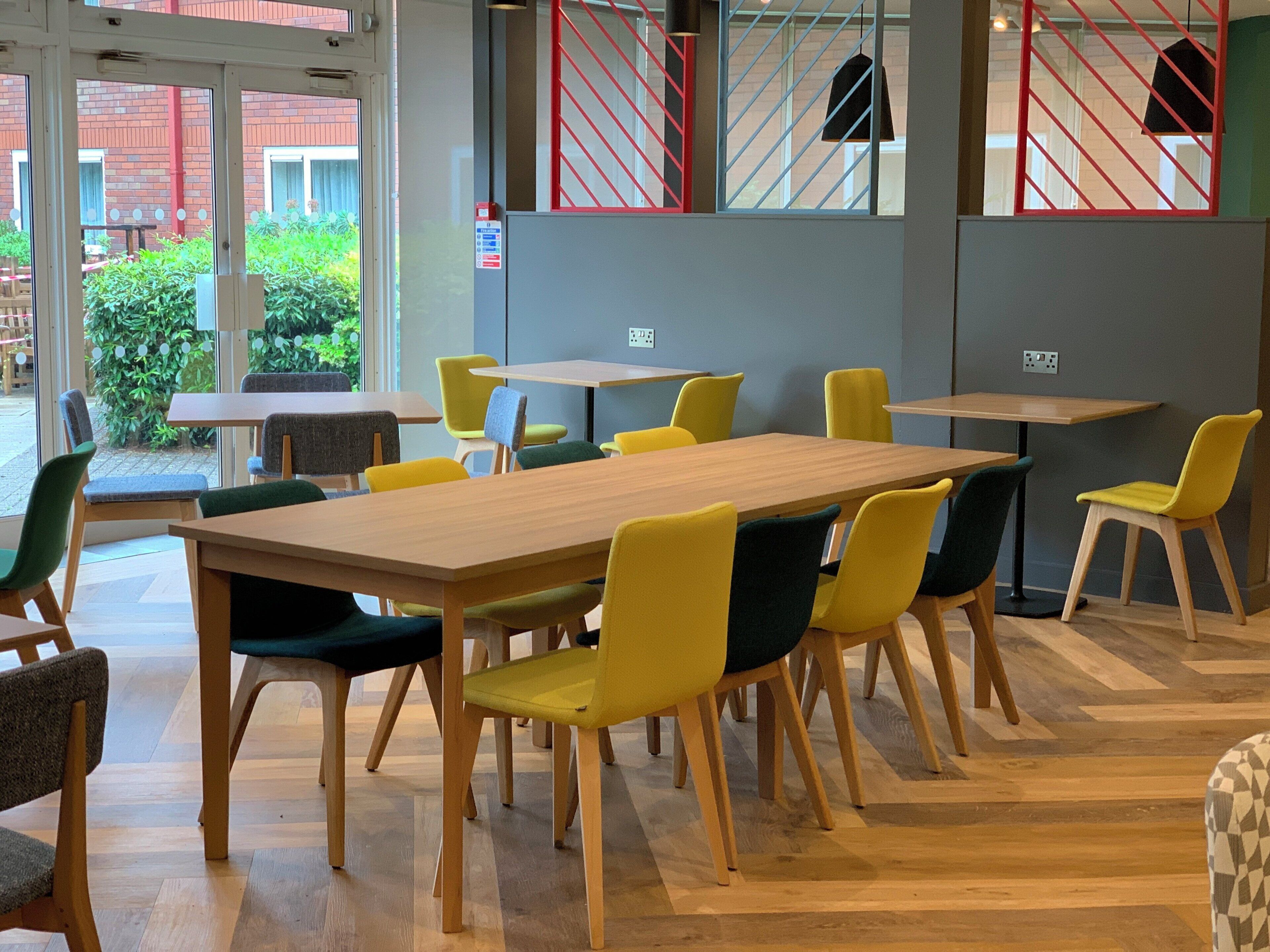 A dining area with wooden tables and chairs, a view of the outside, and a red safety railing.