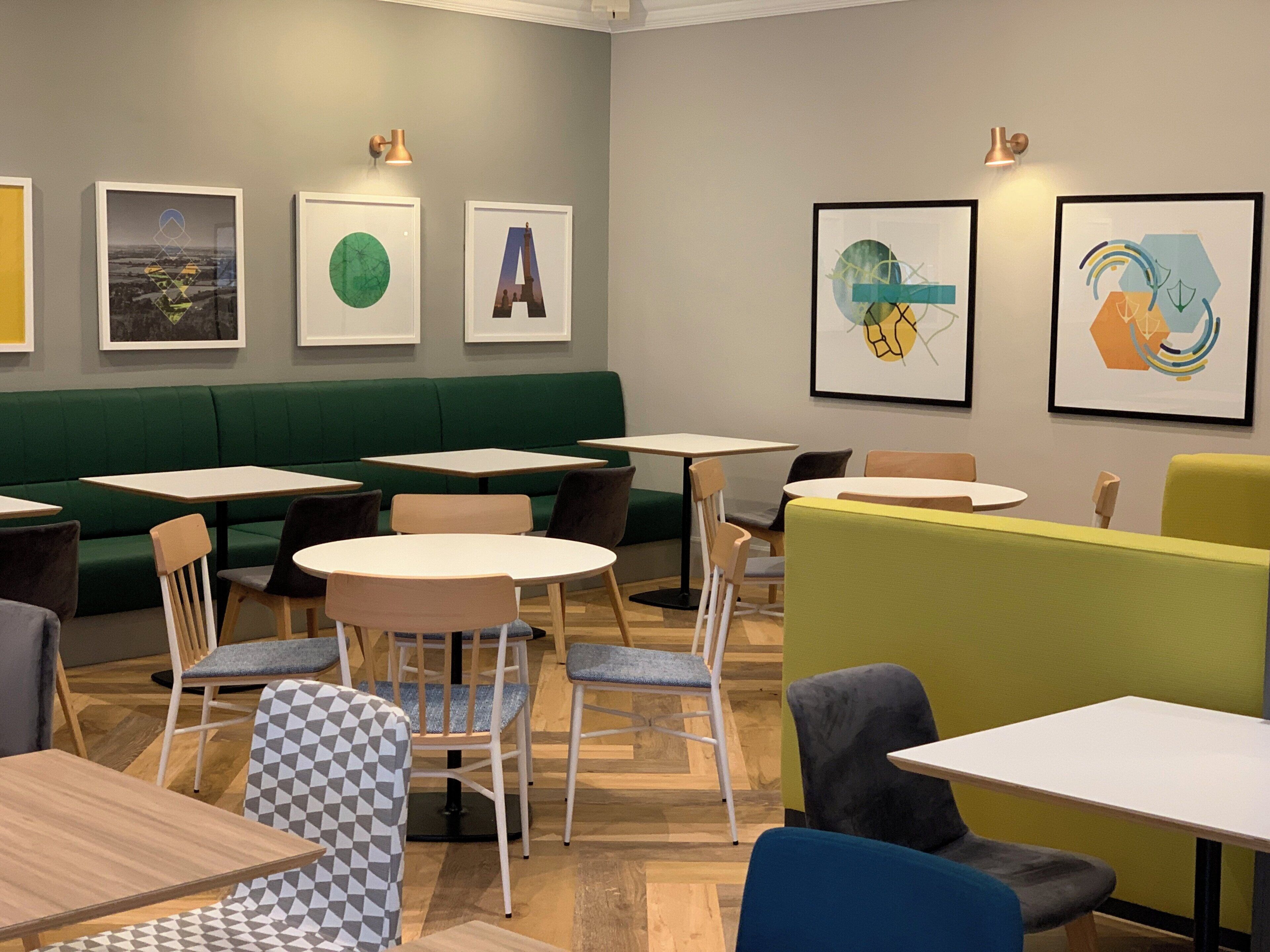 Un café moderno con asientos verdes, mesas blancas y arte abstracto en las paredes.