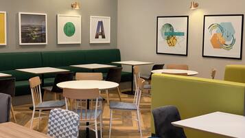 Un café moderno con asientos verdes, mesas blancas y arte abstracto en las paredes.