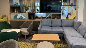 A modern living room with a grey sectional sofa, a wooden coffee table, and a TV mounted on a wall with built-in shelves. - Holiday Inn Aylesbury by IHG (Aylesbury)