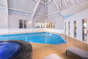 An indoor swimming pool with a tiled floor, a hot tub, and a bench.