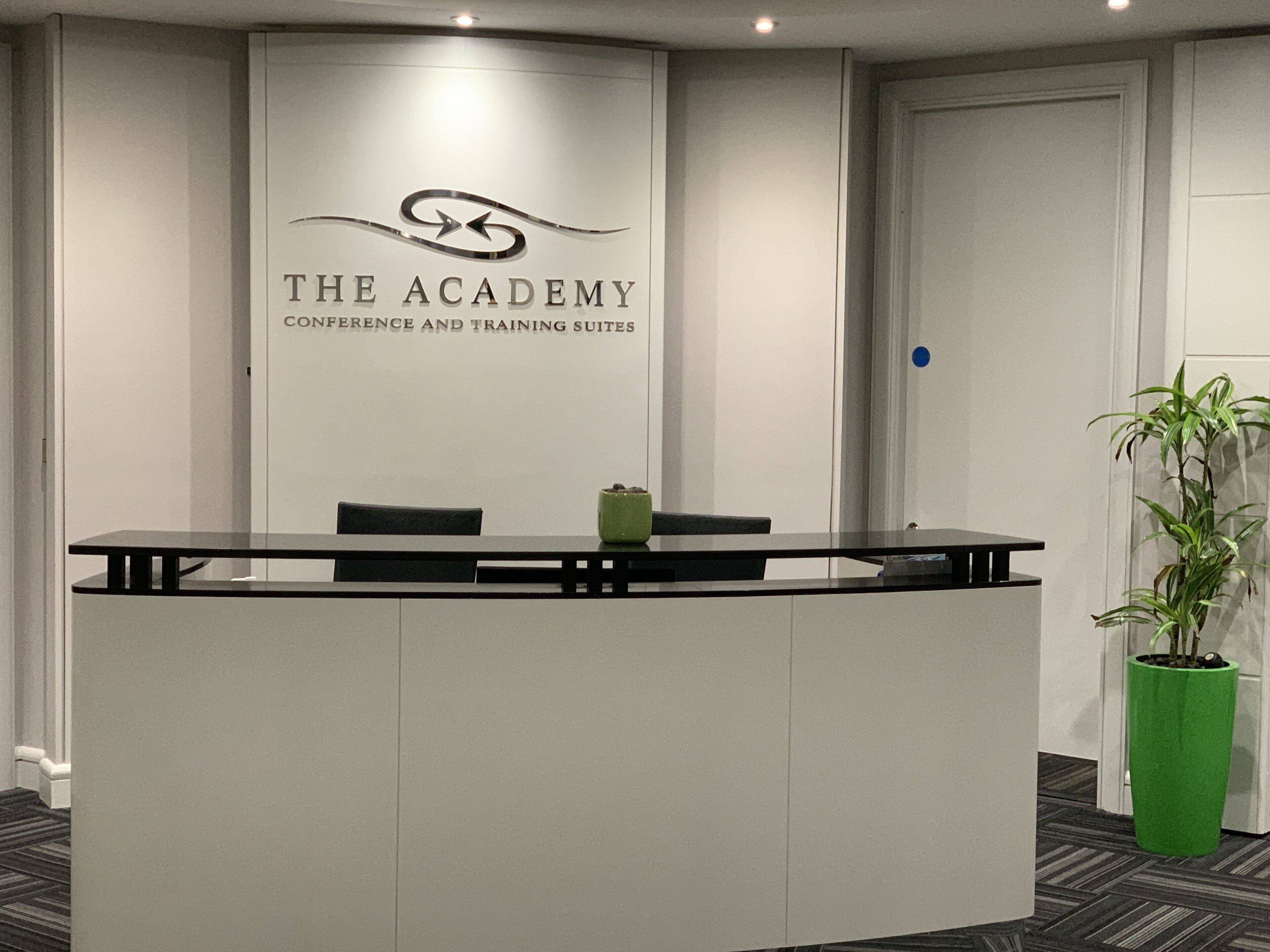A reception desk with a logo above it, a potted plant to the right, and a door in the background.