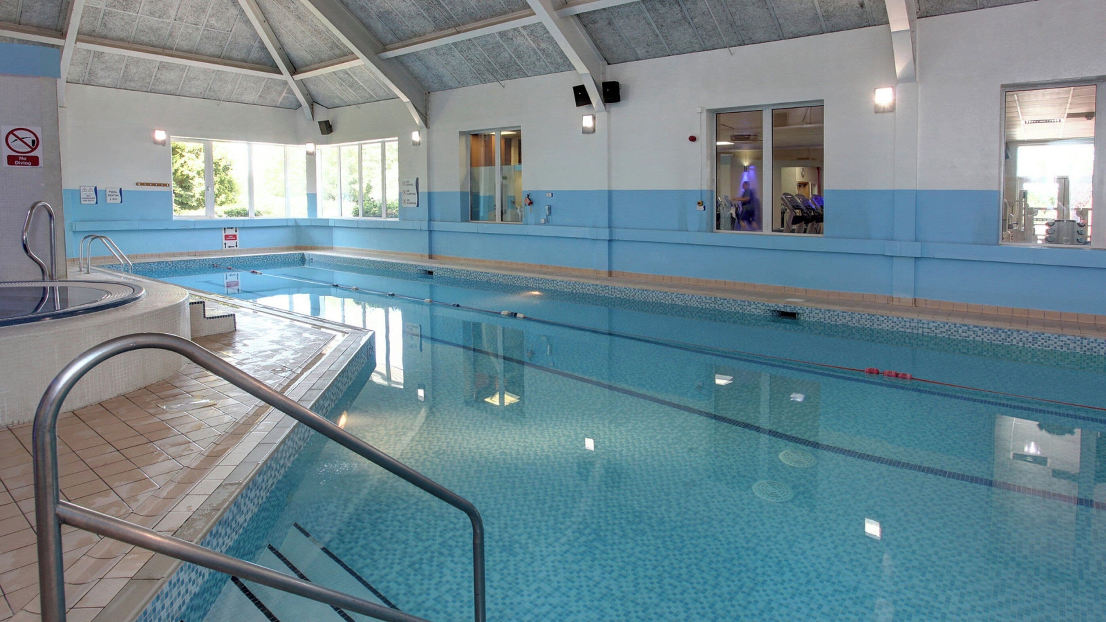 An indoor swimming pool with clear lanes, a diving board, and a tiled floor.