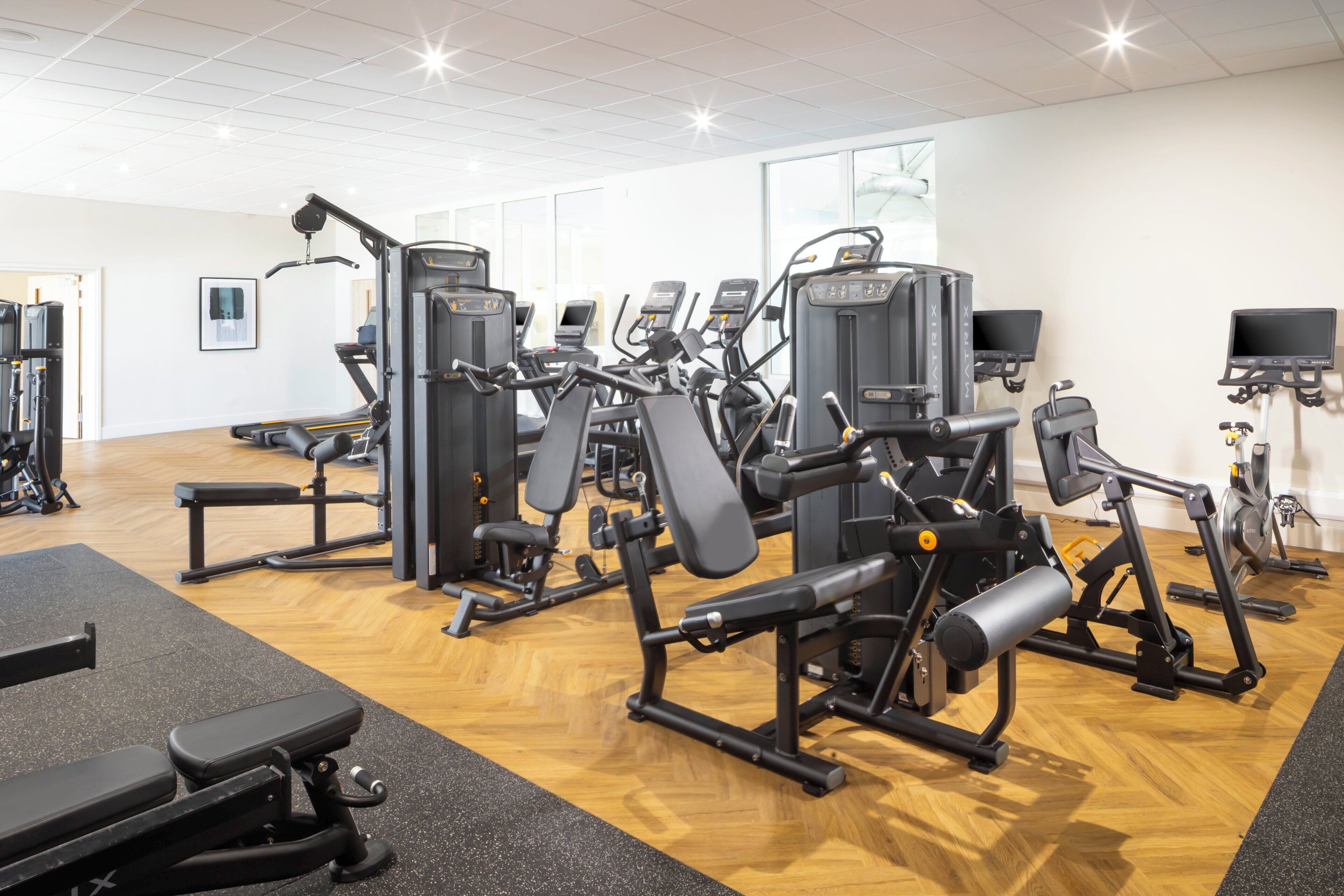 A gym with various exercise machines, a bench, and a TV screen.