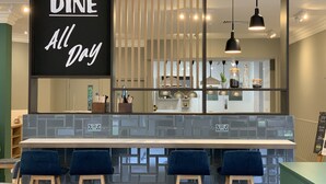 A modern bar area with a sign reading "DINE All Day," featuring a counter with stools and pendant lighting. - Holiday Inn Aylesbury by IHG (Aylesbury)
