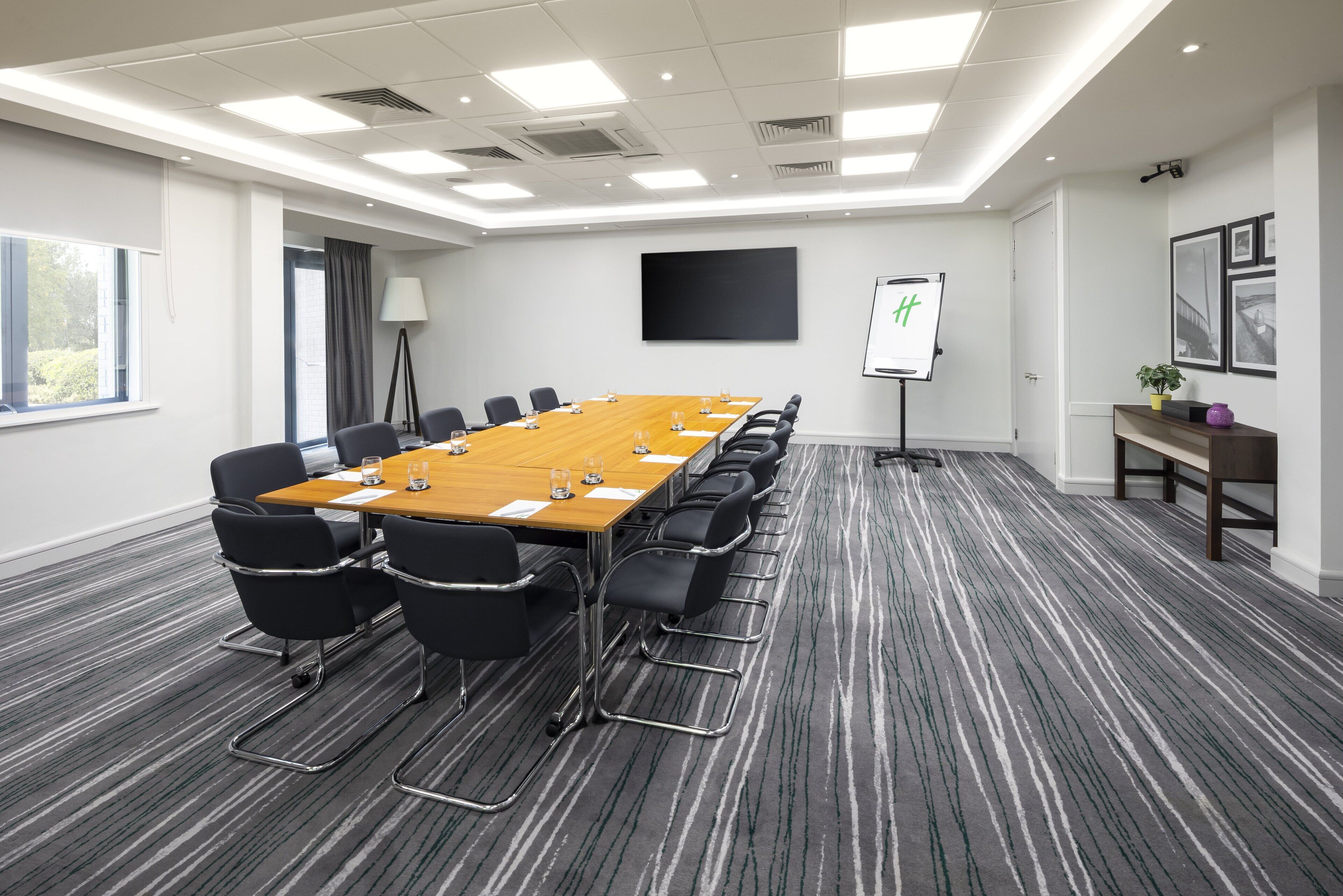 Une salle de conférence équipée d’une longue table, de chaises noires, d’un écran de projection et d’un tableau blanc.