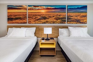 A hotel room with two beds, a wooden headboard, a nightstand with a lamp, and three wall-mounted sunset landscape paintings. - Days Inn by Wyndham Del Rio (Del Rio)