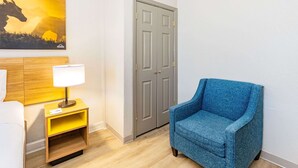 A hotel room with a wooden headboard, a blue armchair, a bedside table with a lamp, and a door with a keyhole.