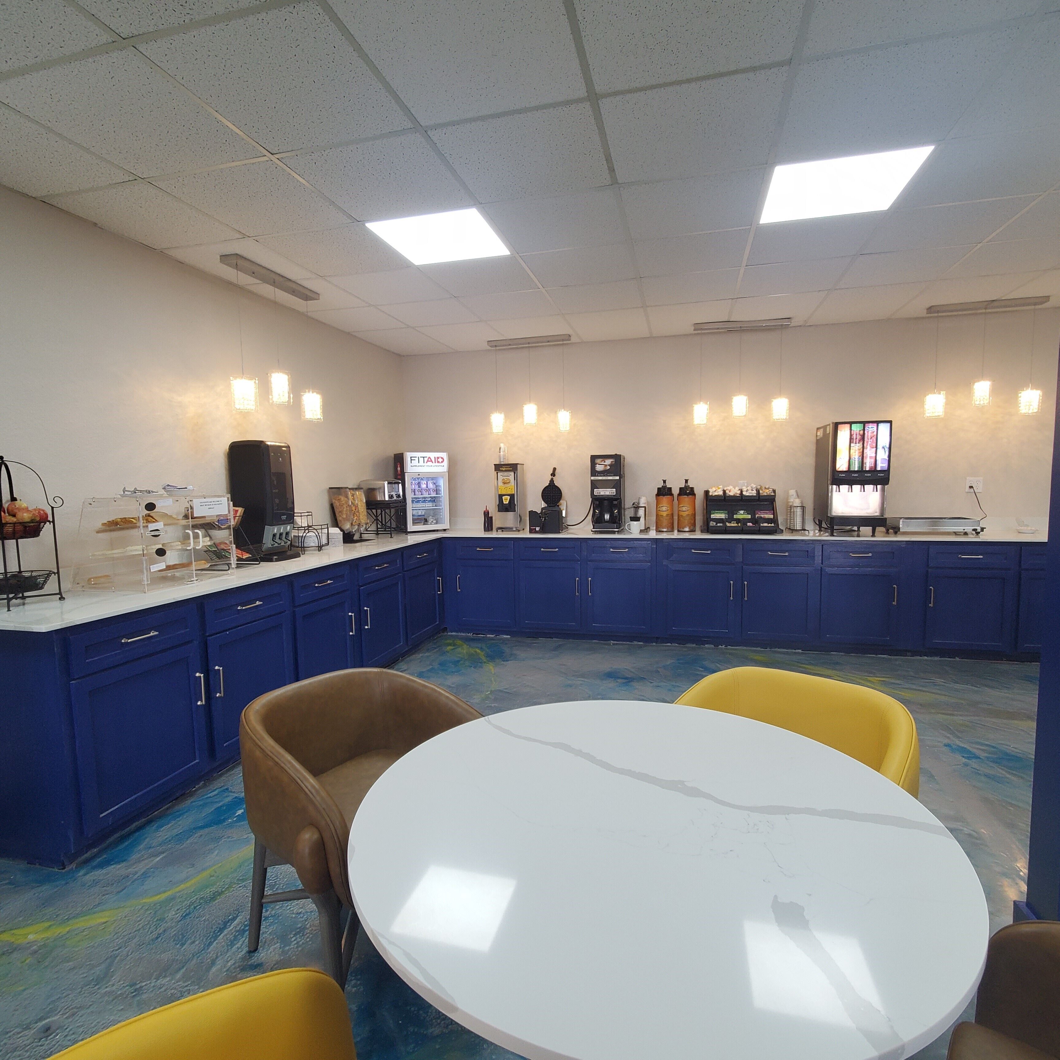 Un salón de conferencias con una mesa blanca, armarios azules y una estación de café.