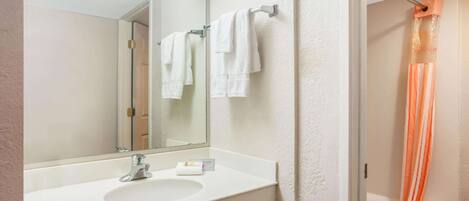Une salle de bain avec un lavabo blanc, un miroir et une douche avec un rideau orange.