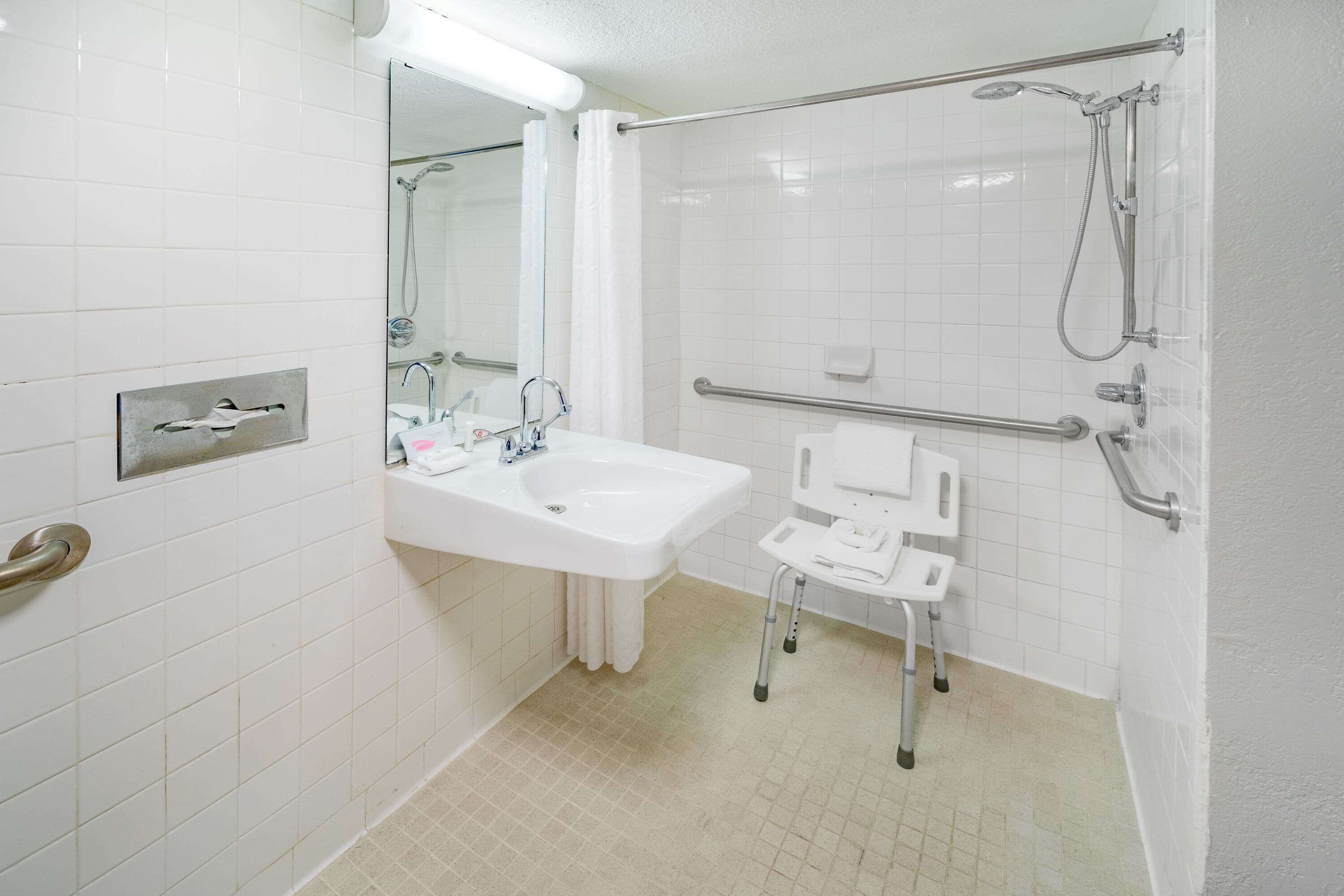 A bathroom with a sink, mirror, shower, and grab bars.