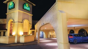 A hotel entrance with a prominent sign, a covered parking area, and a blue car parked inside.