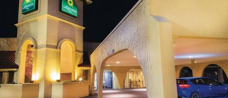 A hotel entrance with a prominent sign, a covered parking area, and a blue car parked inside.