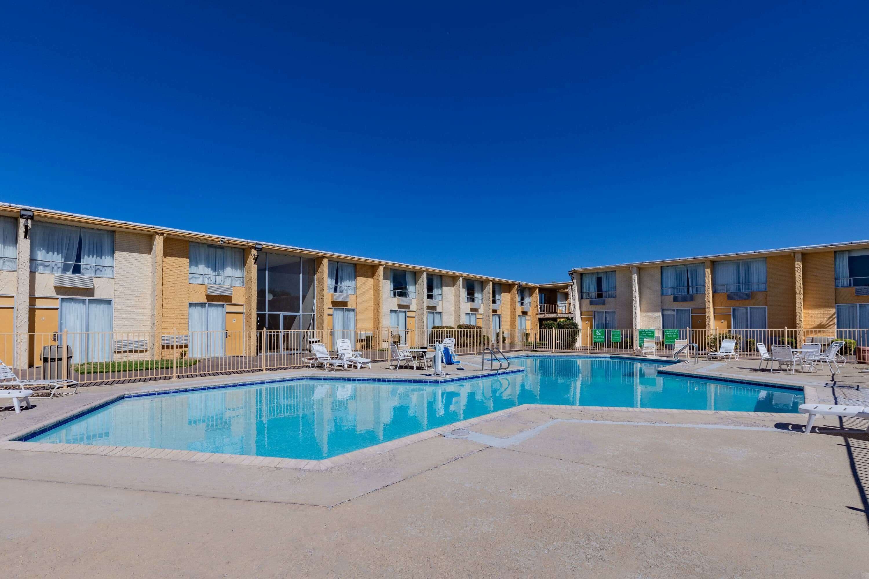 A hotel with a swimming pool, multiple balconies, and a clear blue sky.