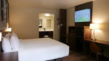 A hotel room with a large bed, a desk with a lamp, a TV, and a mirror.