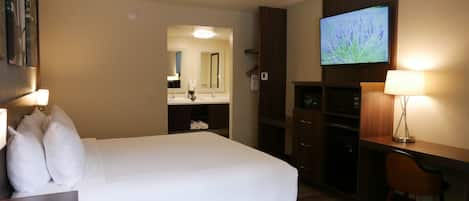 A hotel room with a large bed, a desk with a lamp, a TV, and a mirror.