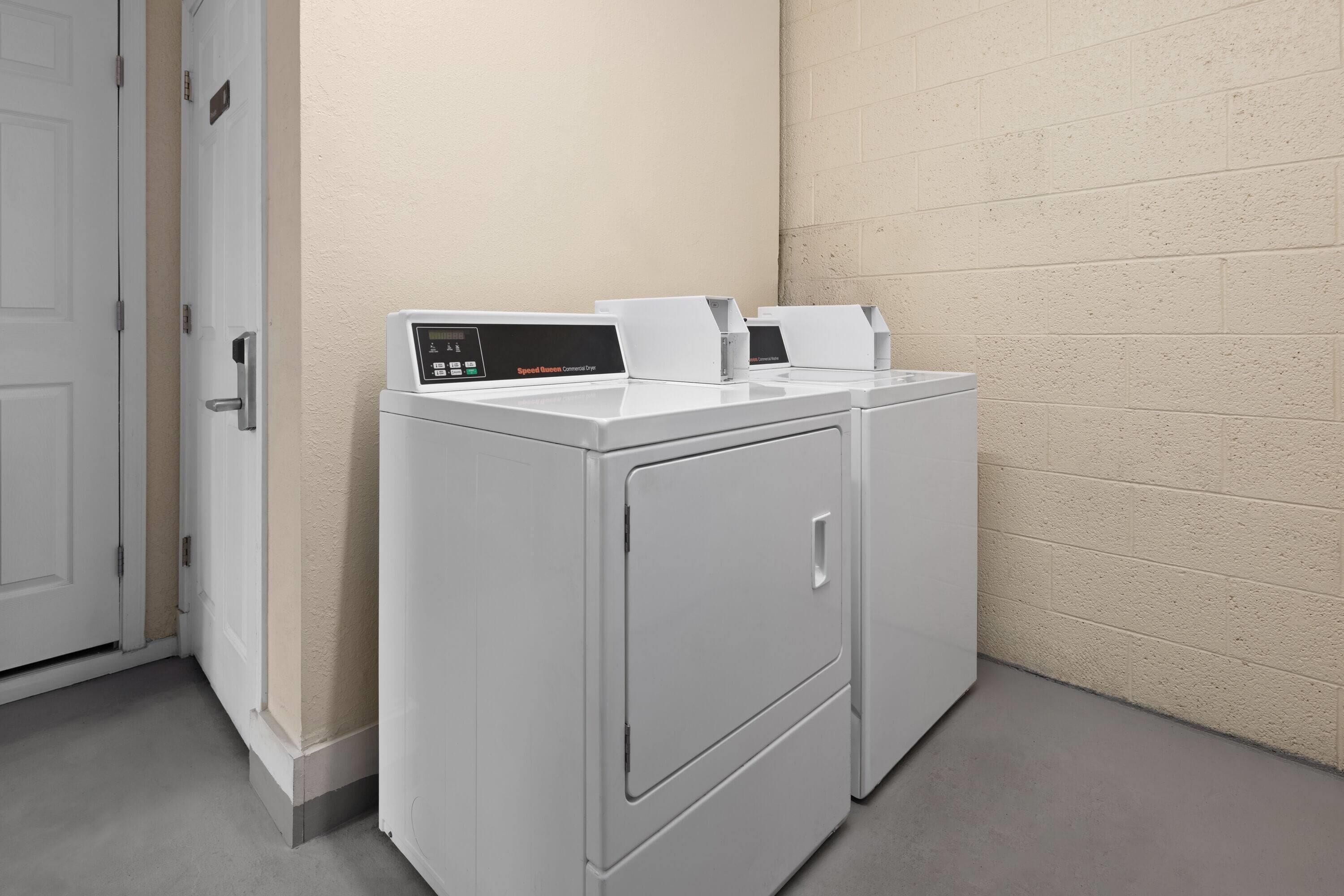 A laundry room with two white front-loading washers and dryers, a beige wall, and a white door.
