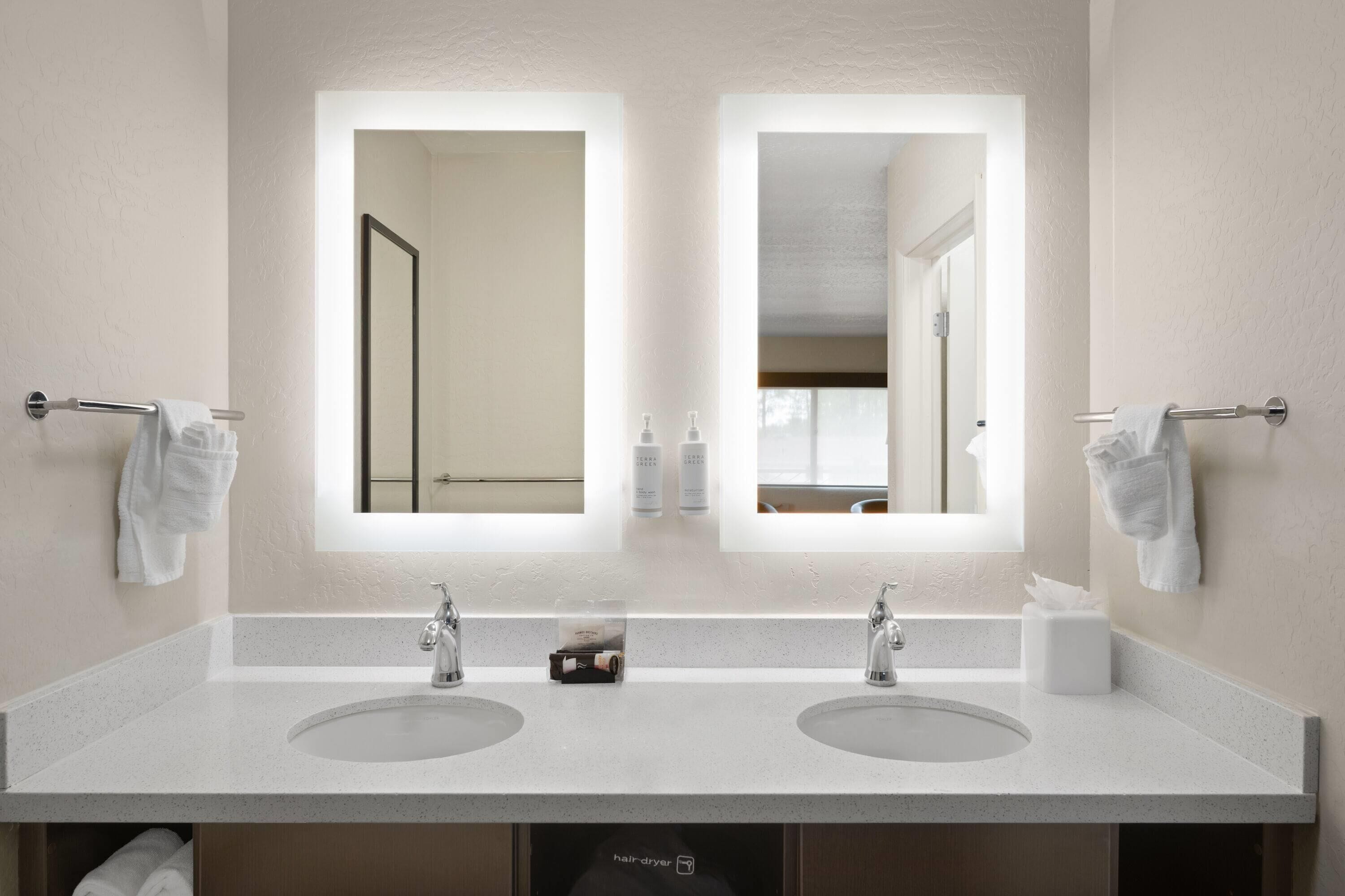 A bathroom with two sinks, a large mirror, and a hair dryer in the cabinet.