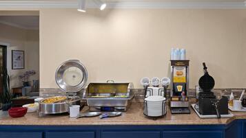 A buffet setup with various food stations including a hot food station, a waffle maker, and a beverage dispenser.