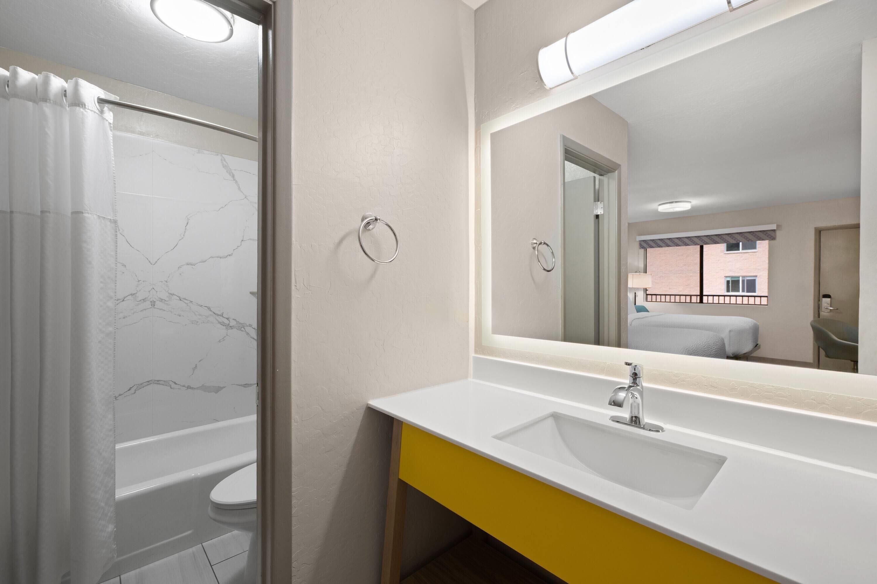 Un baño con una bañera blanca, un tocador amarillo y un espejo grande.