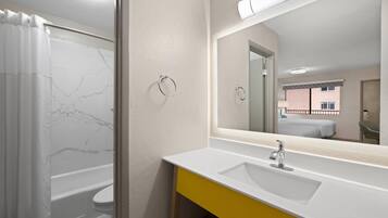 Un baño con una bañera blanca, un tocador amarillo y un espejo grande.